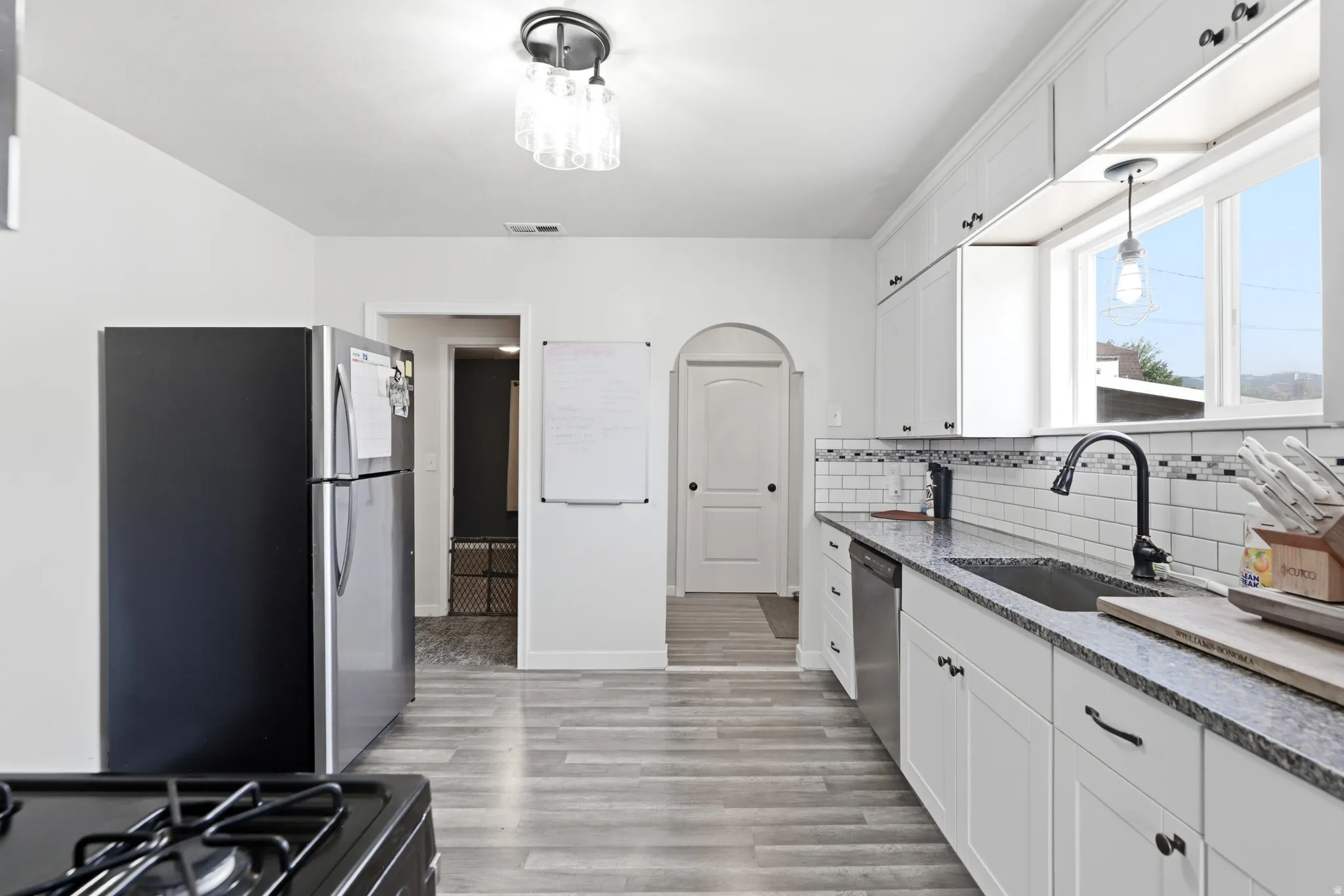 Kitchen featuring white shaker cabinetry, stainless steel appliances, speckled stone countertops, a subway tile backsplash, and wood-finish flooring