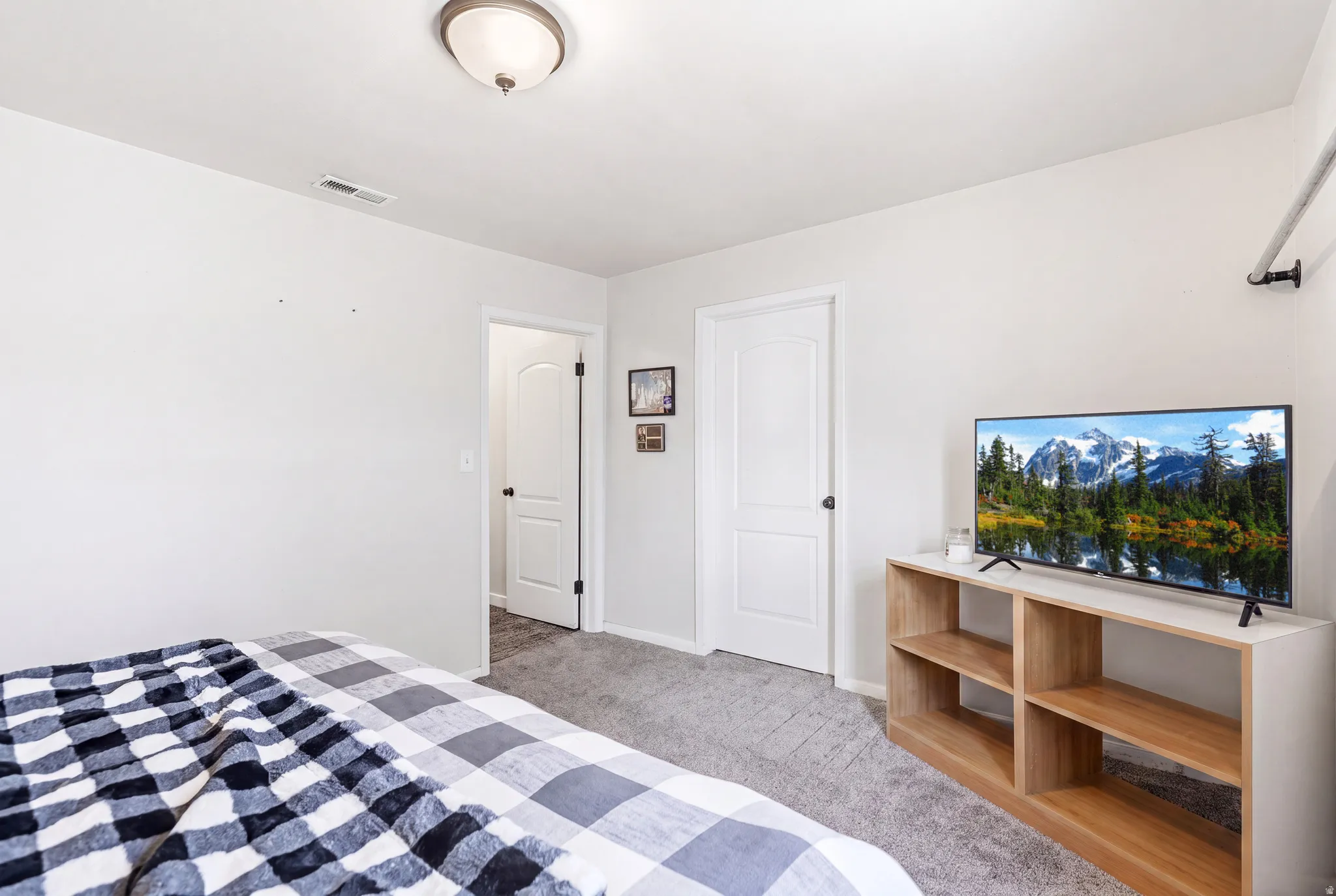 Carpeted bedroom featuring light gray walls, a flush-mount ceiling light fixture, and two interior doors with black hardware