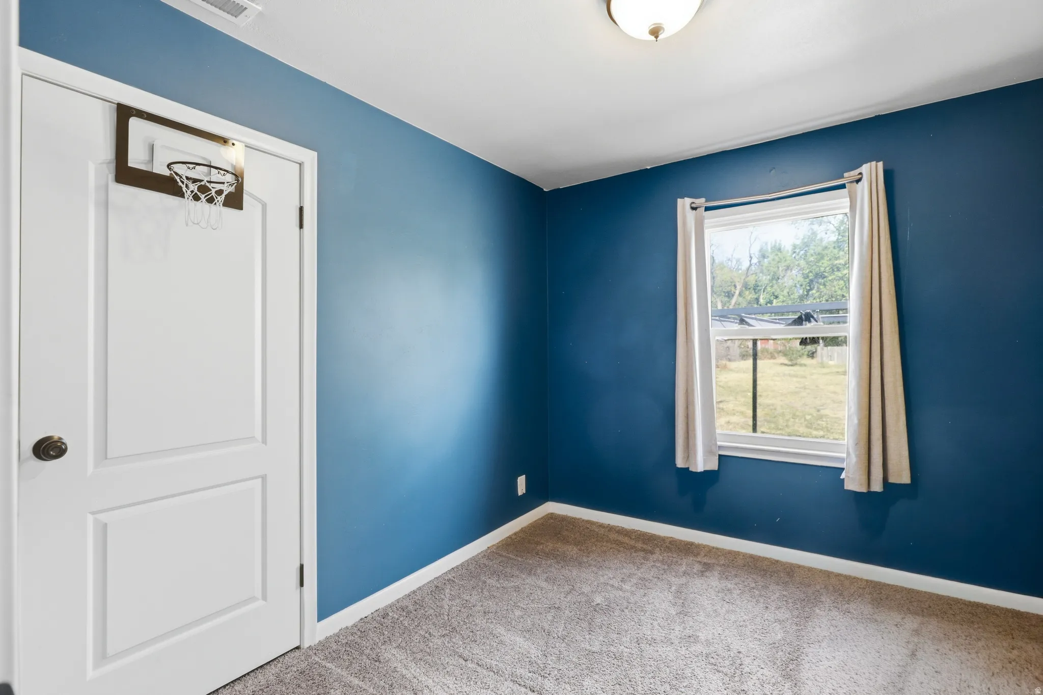 Room featuring a single window with a framed outdoor view, blue painted walls, and carpet flooring