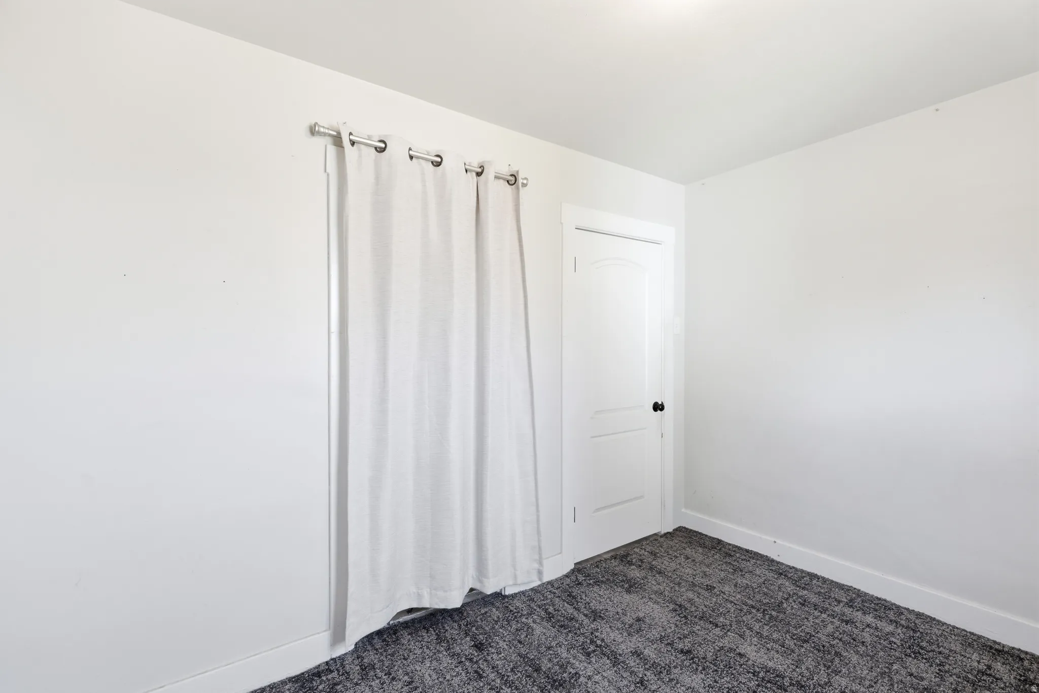 Room featuring light-colored walls and dark patterned carpeting
