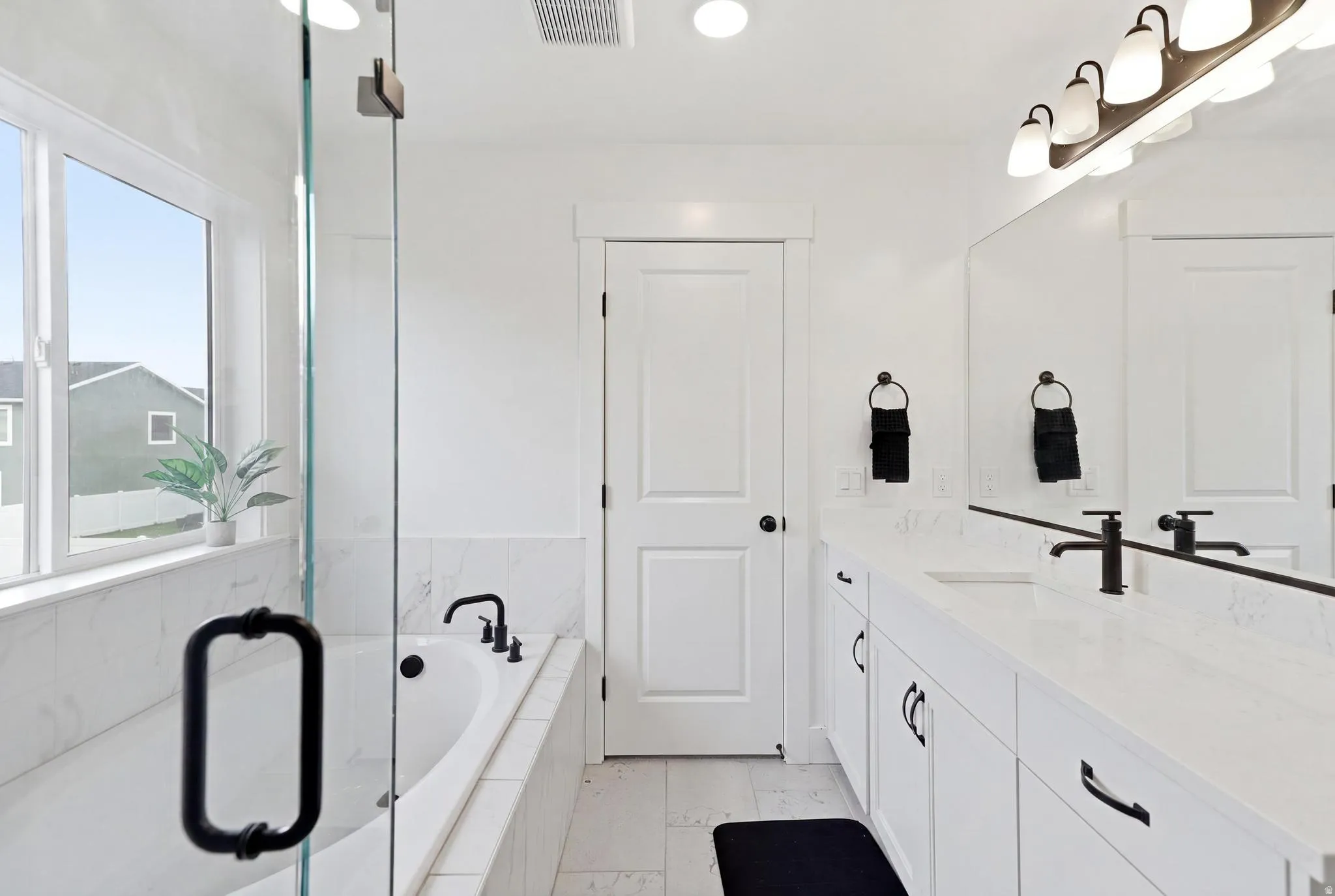 Bathroom featuring a built-in soaking tub, glass-enclosed shower, dual vanity with undermount sinks, and matte black fixtures