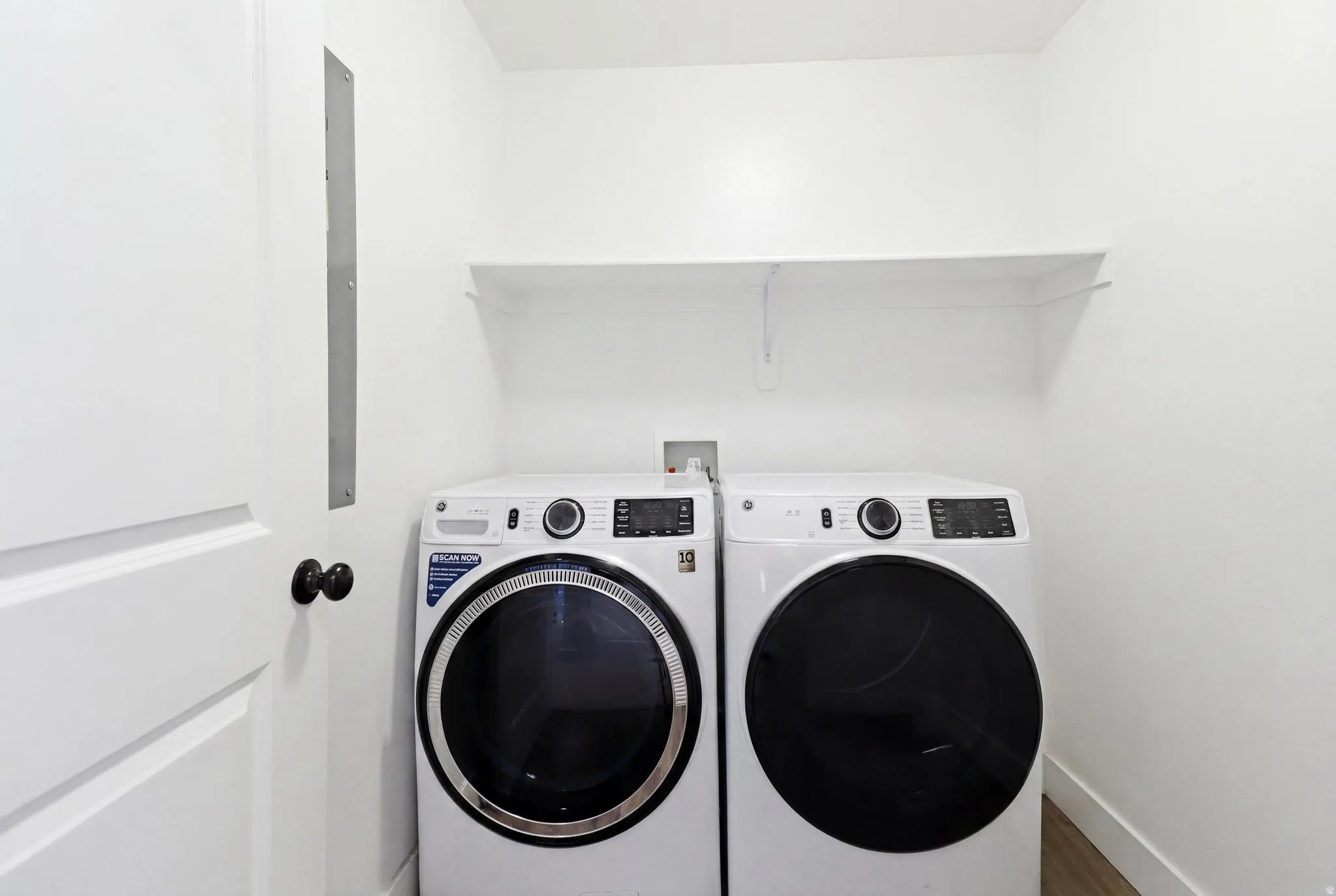 Dedicated laundry area featuring a built-in shelving unit, white walls, and wood-finish flooring