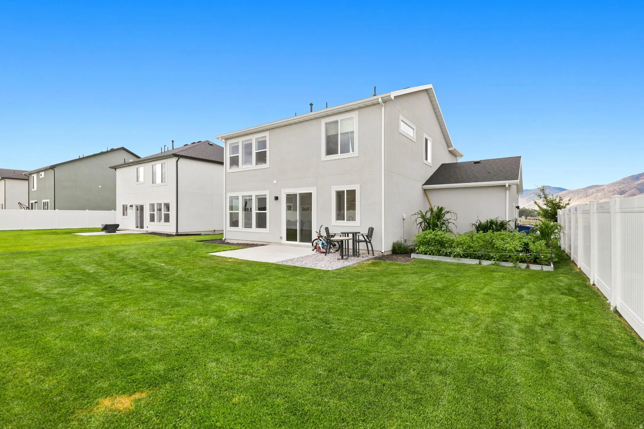 Expansive green lawn with a white vinyl privacy fence, a concrete patio, and a raised garden bed
