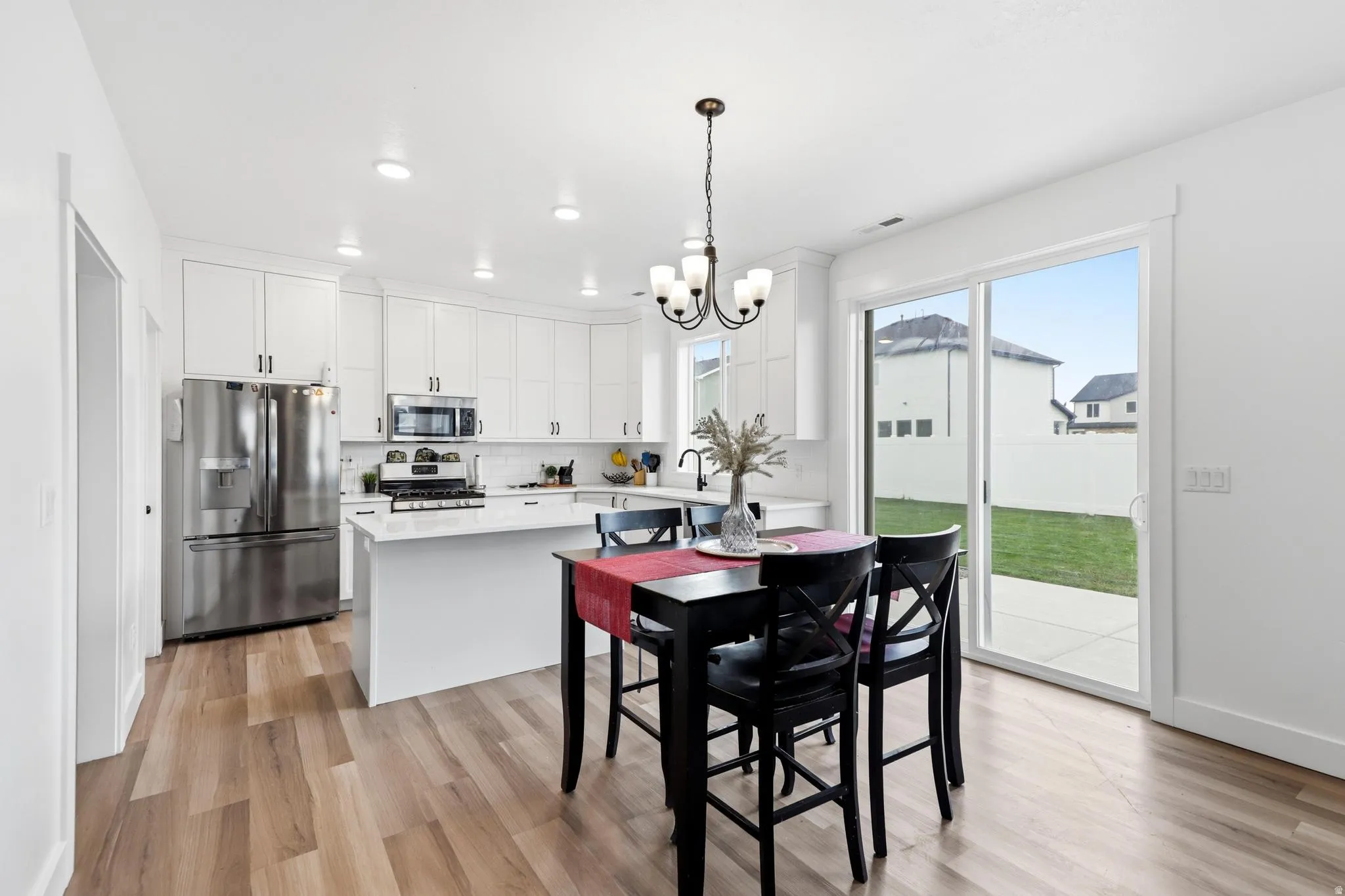 Kitchen and dining area featuring wood-finish flooring, white cabinetry, stainless steel appliances, a center island with a white countertop, and a sliding glass door to the backyard patio