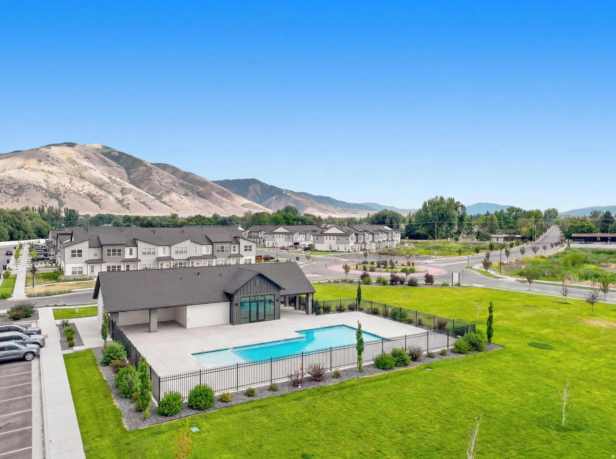 Community amenities featuring a rectangular swimming pool, a modern clubhouse with dark siding and large windows, and a paved parking area