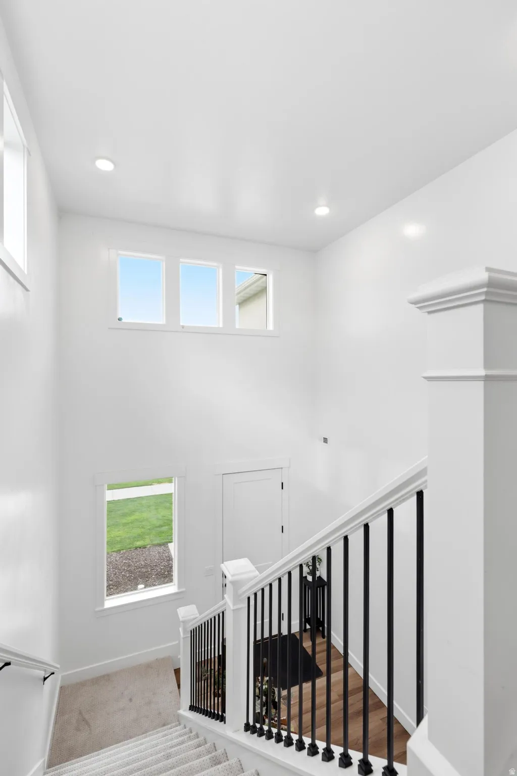 Two-story foyer featuring a contemporary staircase with black wrought iron spindles and white newel posts, high ceilings, recessed lighting, and multiple windows