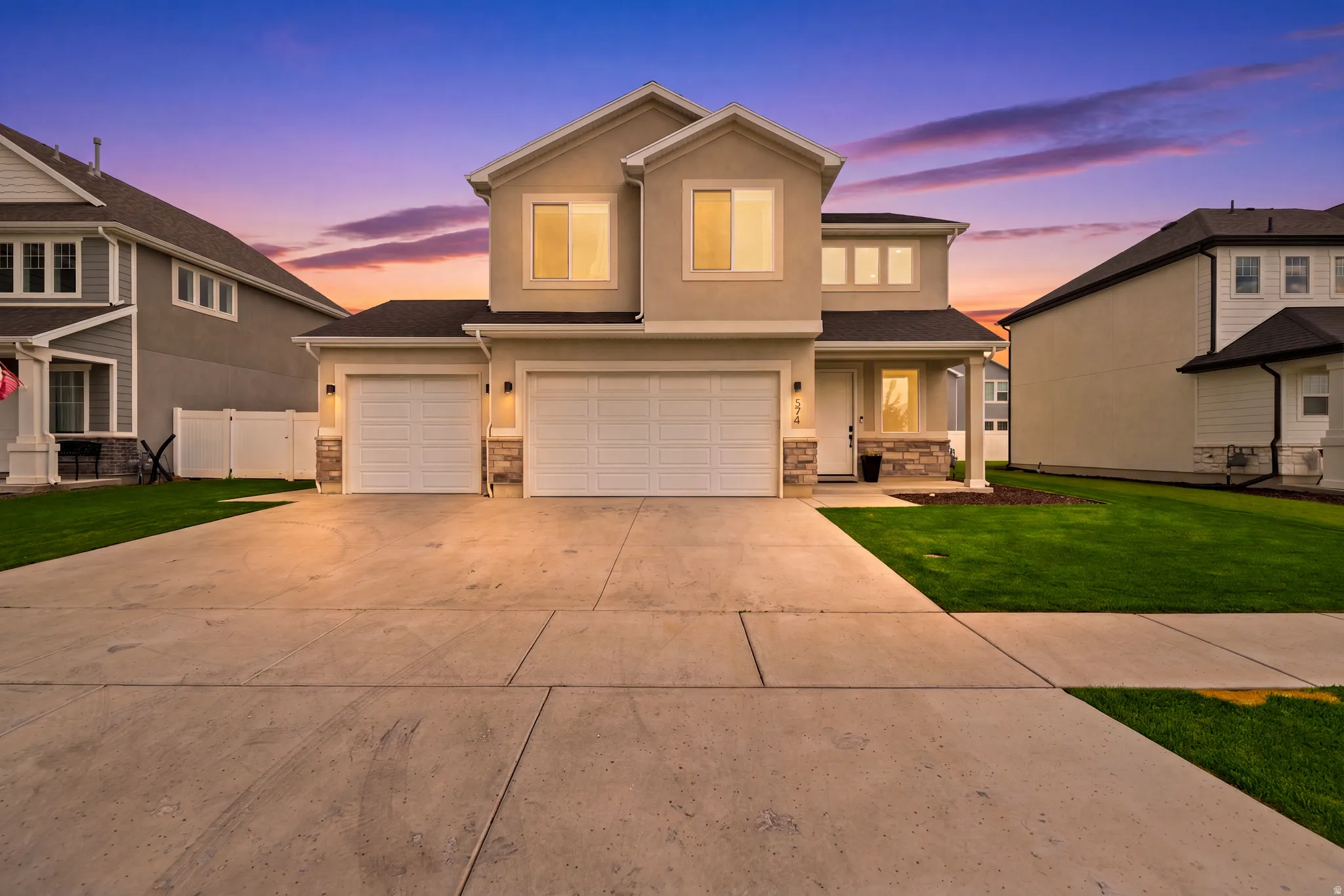 Two-story stucco exterior with stone accents, a concrete driveway, two garage doors, and a covered front porch