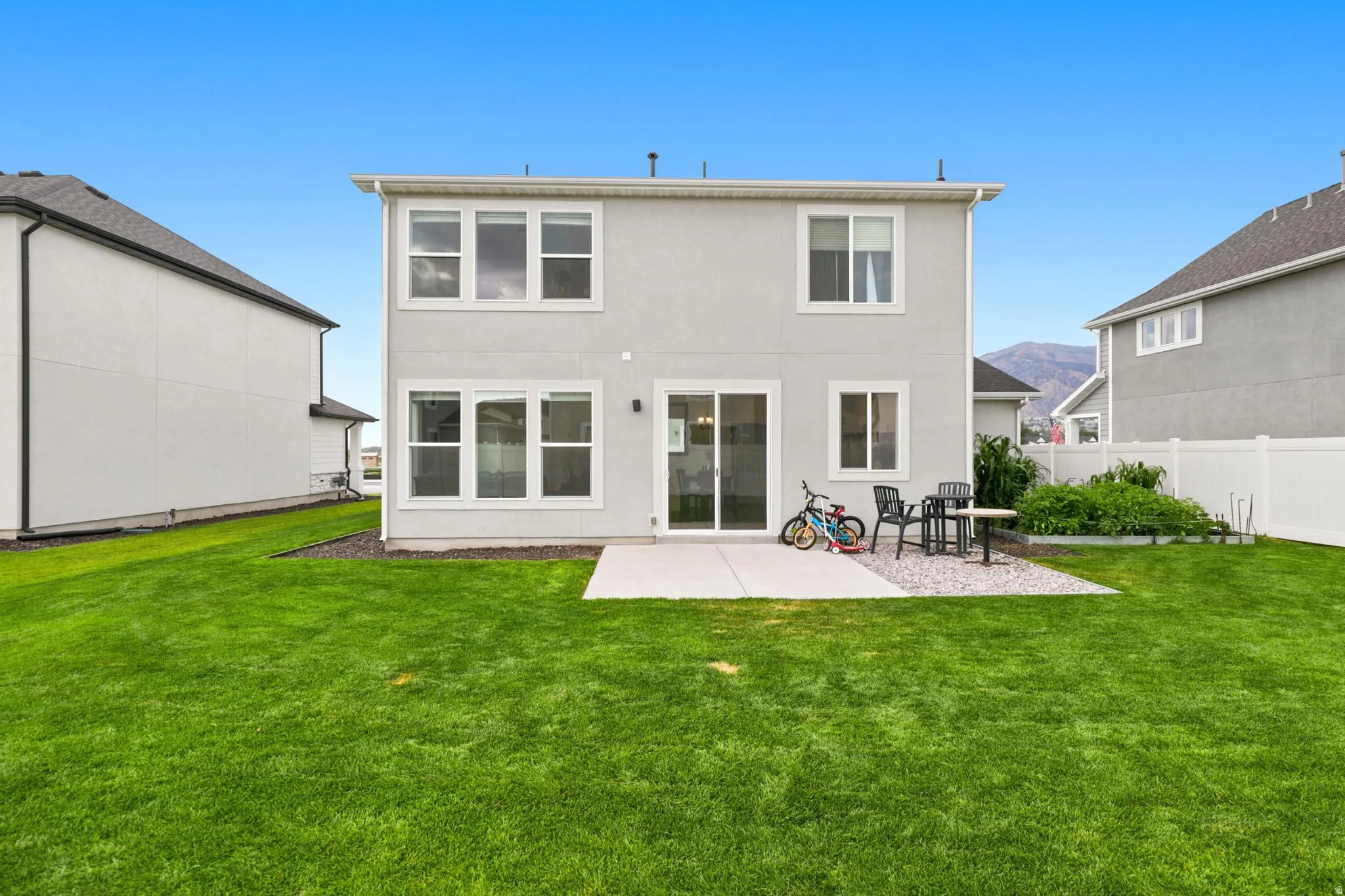 Spacious backyard featuring a concrete patio, expansive lawn, and a white privacy fence