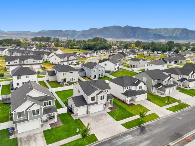 Residential neighborhood featuring contemporary two-story homes with attached garages, manicured lawns, and white perimeter fencing, set against a mountain backdrop