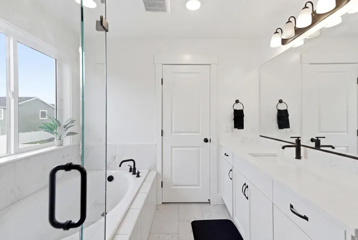 Bathroom featuring a built-in soaking tub, glass-enclosed shower, dual vanity with undermount sinks, and matte black fixtures