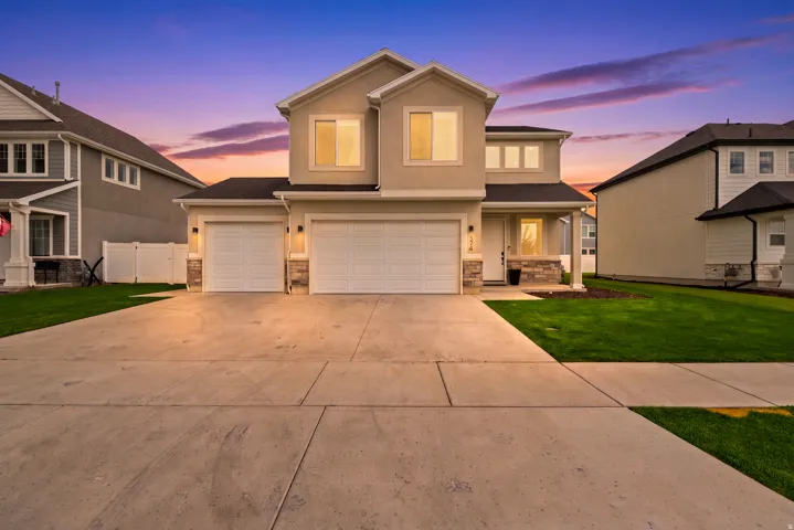 Two-story stucco exterior with stone accents, a concrete driveway, two garage doors, and a covered front porch