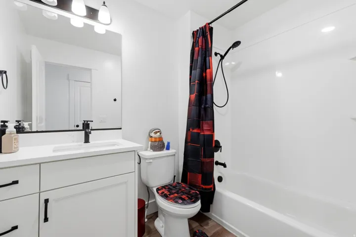 Full bathroom featuring a white vanity with integrated sink, matte black fixtures, a contemporary vanity light, a bathtub with a shower, and wood-finish flooring