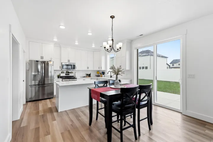 Kitchen and dining area featuring wood-finish flooring, white cabinetry, stainless steel appliances, a center island with a white countertop, and a sliding glass door to the backyard patio
