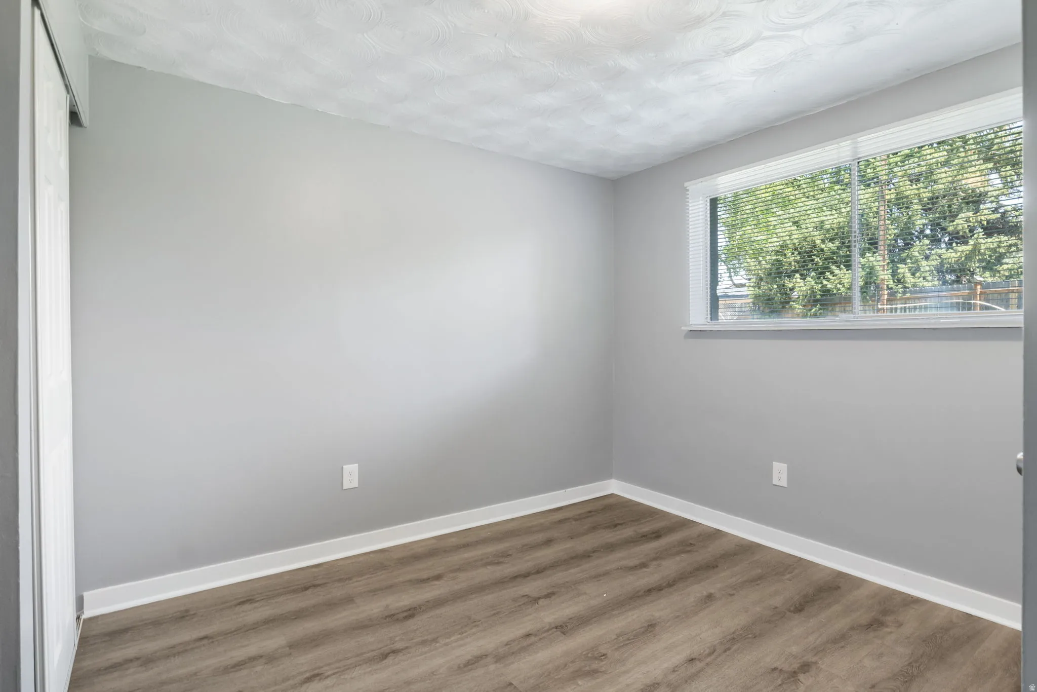 Room featuring a neutral gray color palette, wood-finish flooring, white baseboards, and a window with blinds