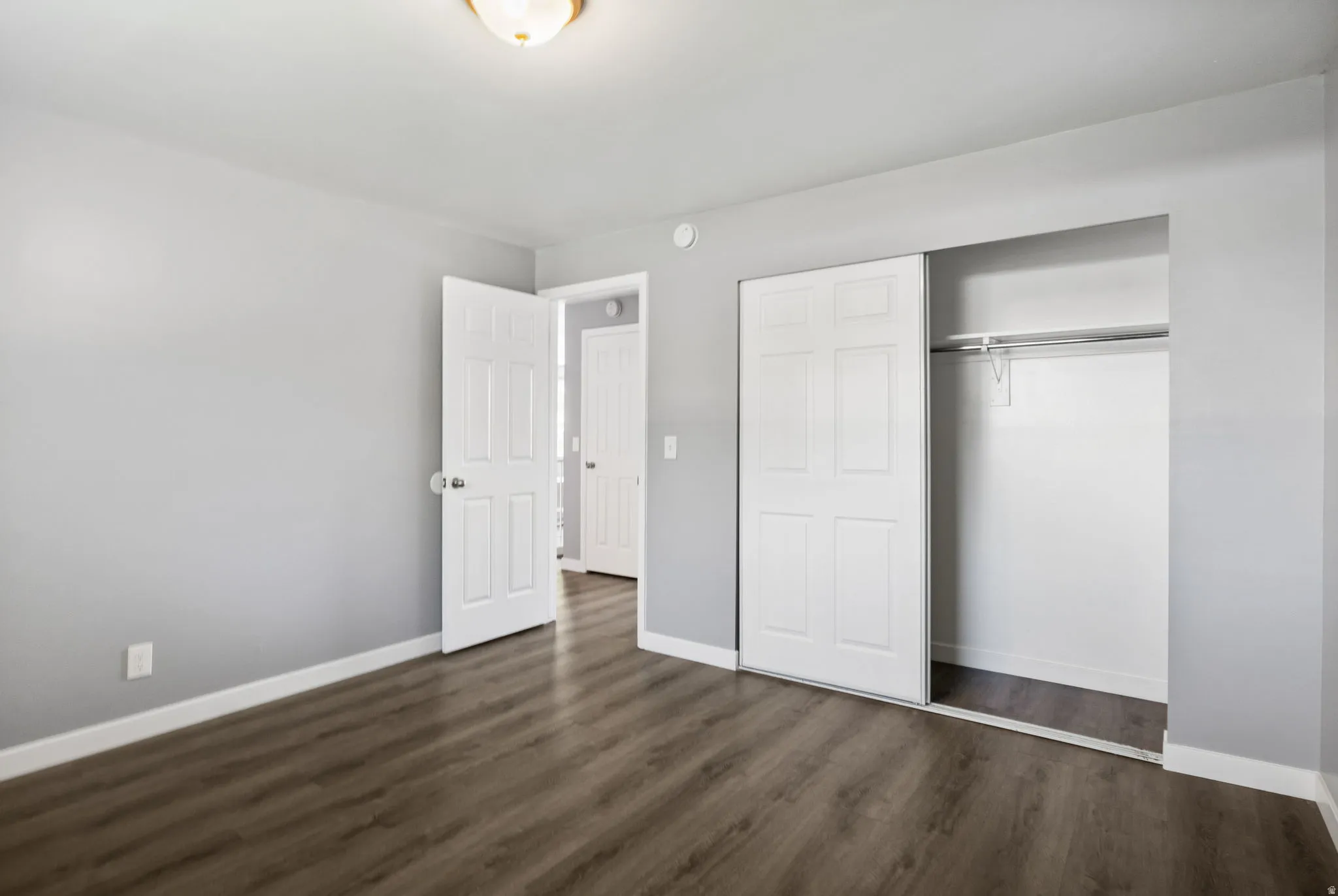 Bedroom featuring wood-finish flooring, light gray wall paint, white baseboards, and a built-in closet with sliding bifold doors