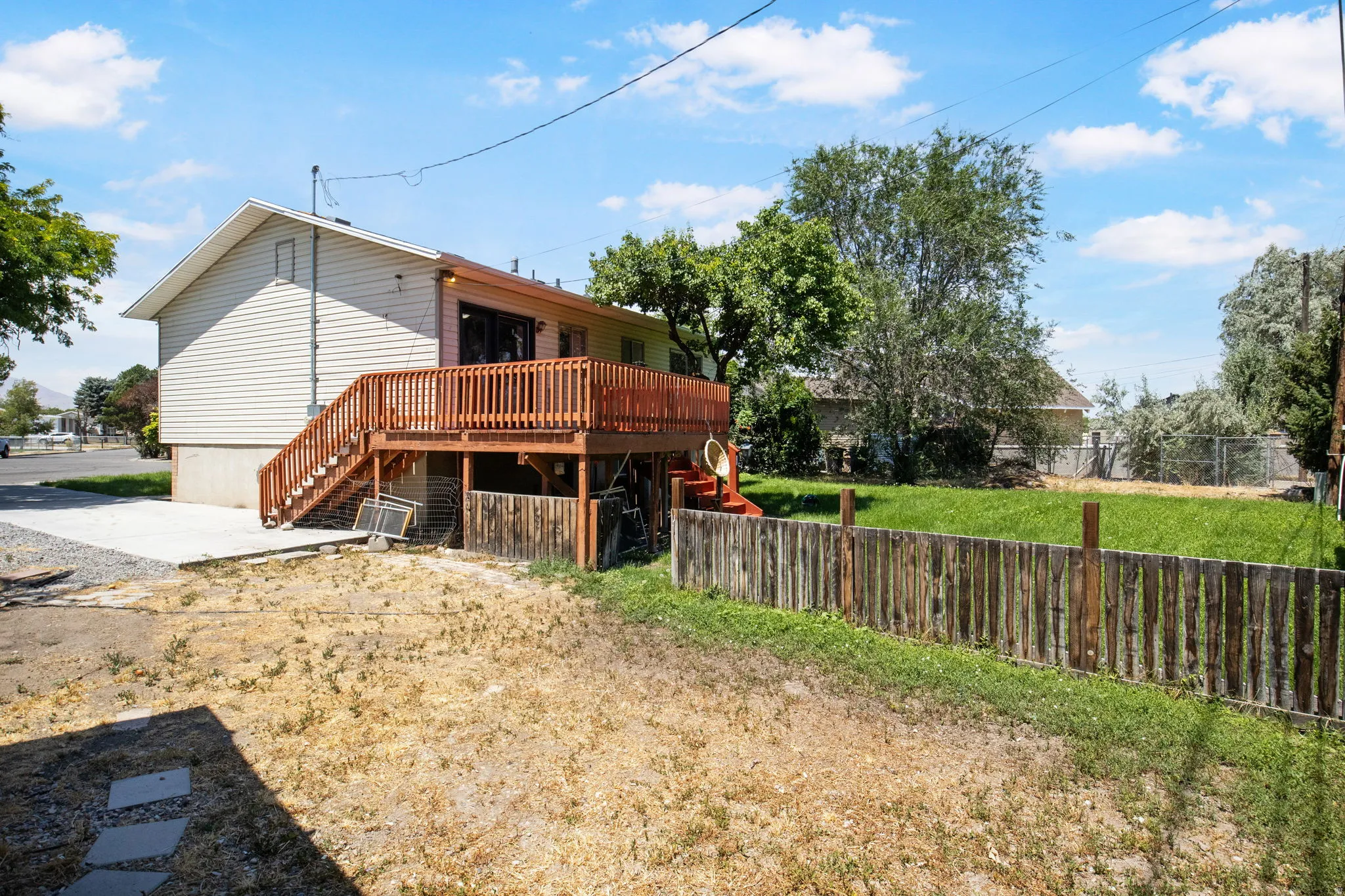 Rear exterior featuring a spacious wood deck with stairs, a concrete patio, and a partial wood fence defining the property boundary