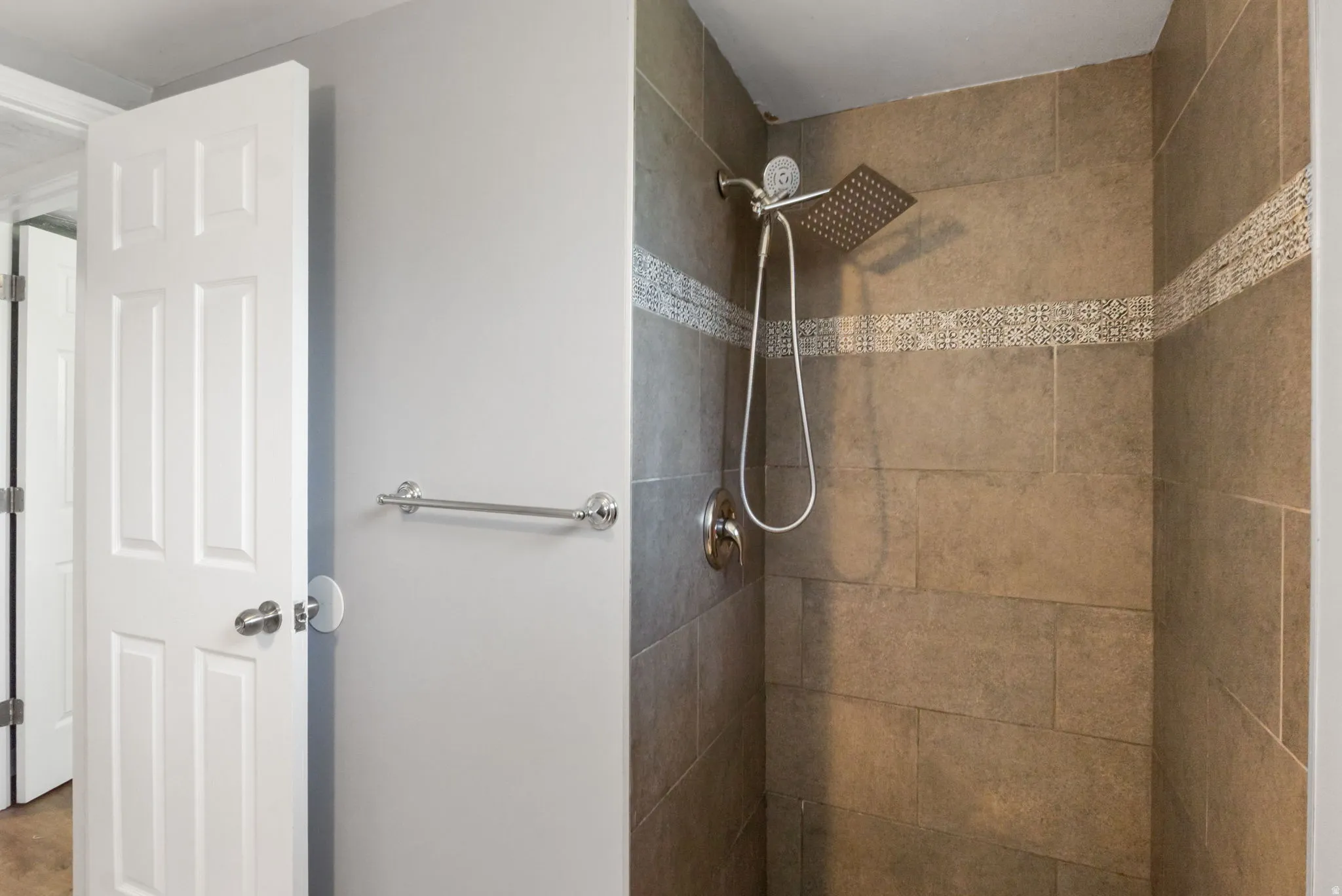 Shower enclosure featuring large format tile and a decorative mosaic accent band