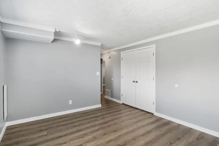 Room featuring wood-finish flooring, light grey painted walls, white baseboards, and white crown molding
