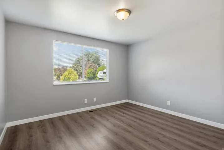 Room featuring a large window with horizontal blinds, grey wall paint, white baseboards, and wood-finish flooring