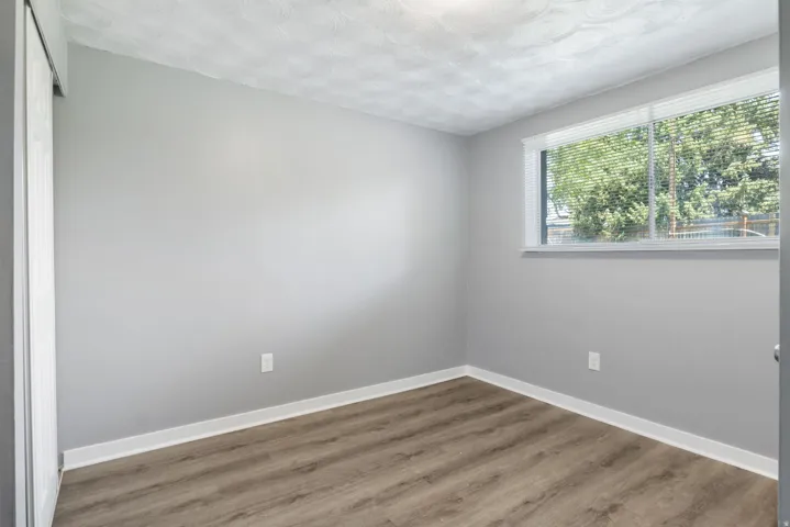 Room featuring a neutral gray color palette, wood-finish flooring, white baseboards, and a window with blinds