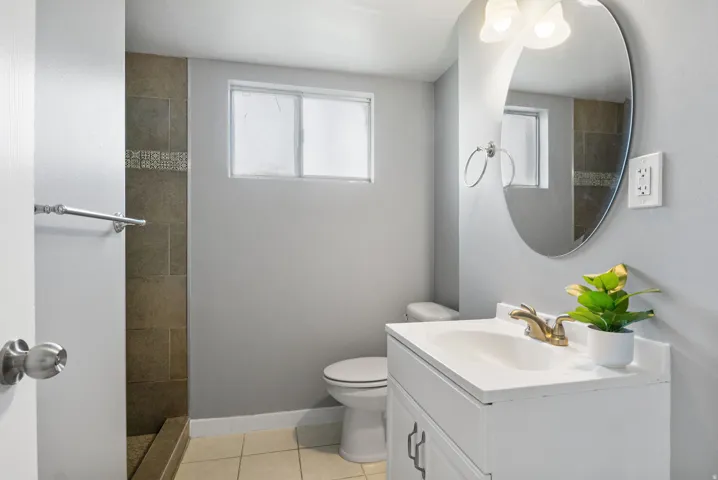 Bathroom featuring a white vanity with integrated sink, brass-finish faucet, and an oval wall mirror with overhead lighting