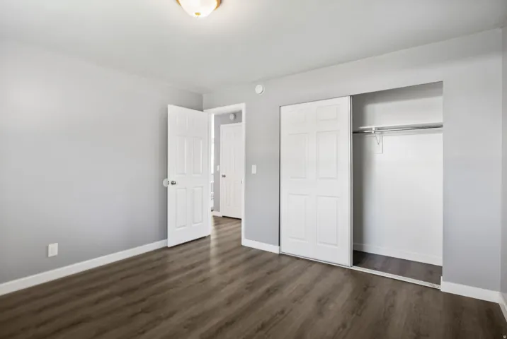 Bedroom featuring wood-finish flooring, light gray wall paint, white baseboards, and a built-in closet with sliding bifold doors