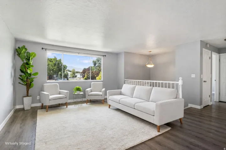 Spacious interior featuring a wide picture window, wood-finish flooring, a white spindle railing, and a brass-finish pendant light fixture