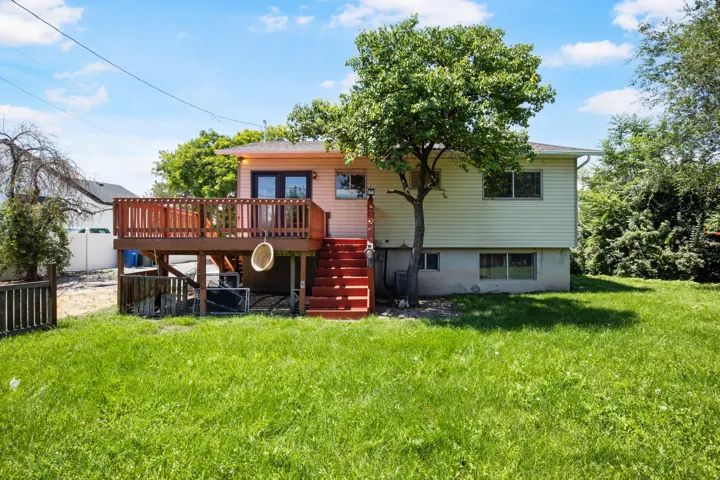 Expansive backyard featuring a large wood deck with railings, exterior stairs, and a mature tree