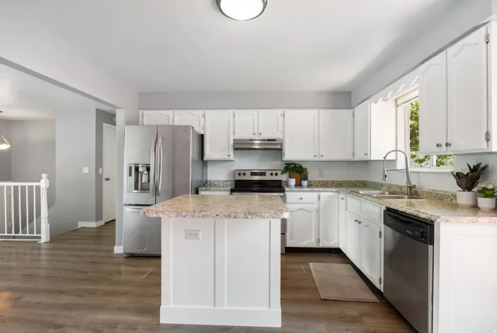 Spacious kitchen featuring white cabinetry, stone-finish countertops, stainless steel appliances, a center island with breakfast bar seating, and wood-finish flooring