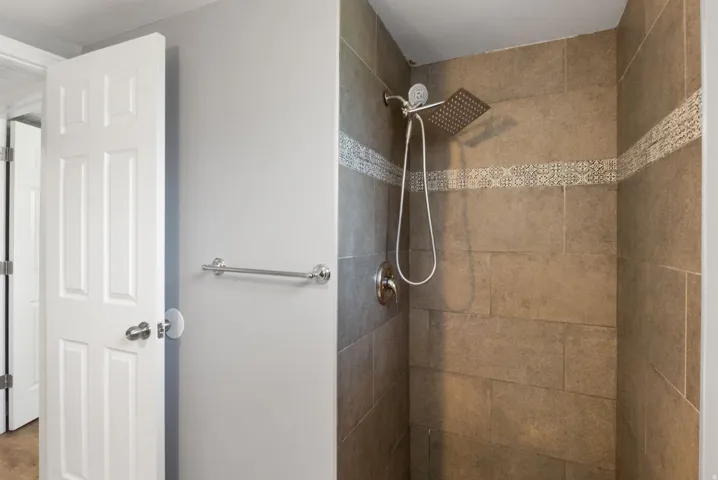 Shower enclosure featuring large format tile and a decorative mosaic accent band