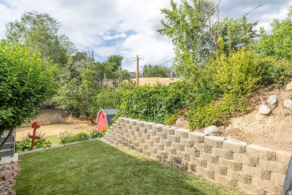 Terraced backyard with a retaining wall, green lawn, and mature plantings