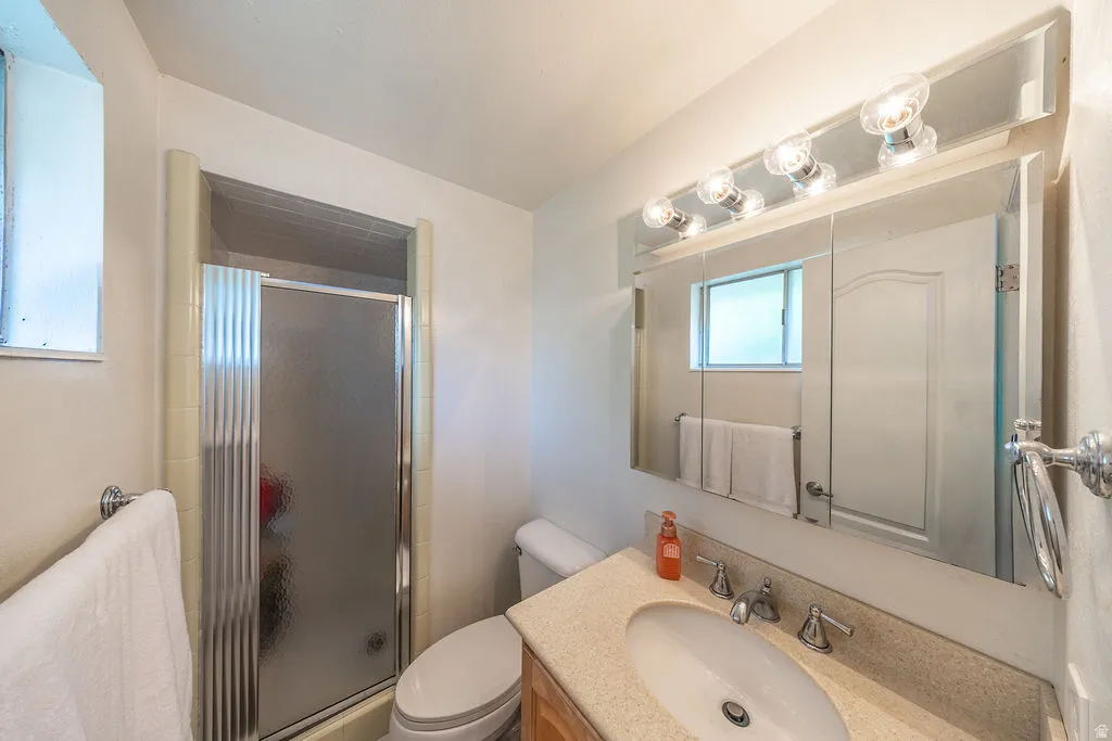 Master bathroom featuring a built-in shower with sliding frosted glass doors, a vanity with a light-toned countertop and integrated sink, a wall-mounted mirror cabinet, and a five-bulb vanity light fixture