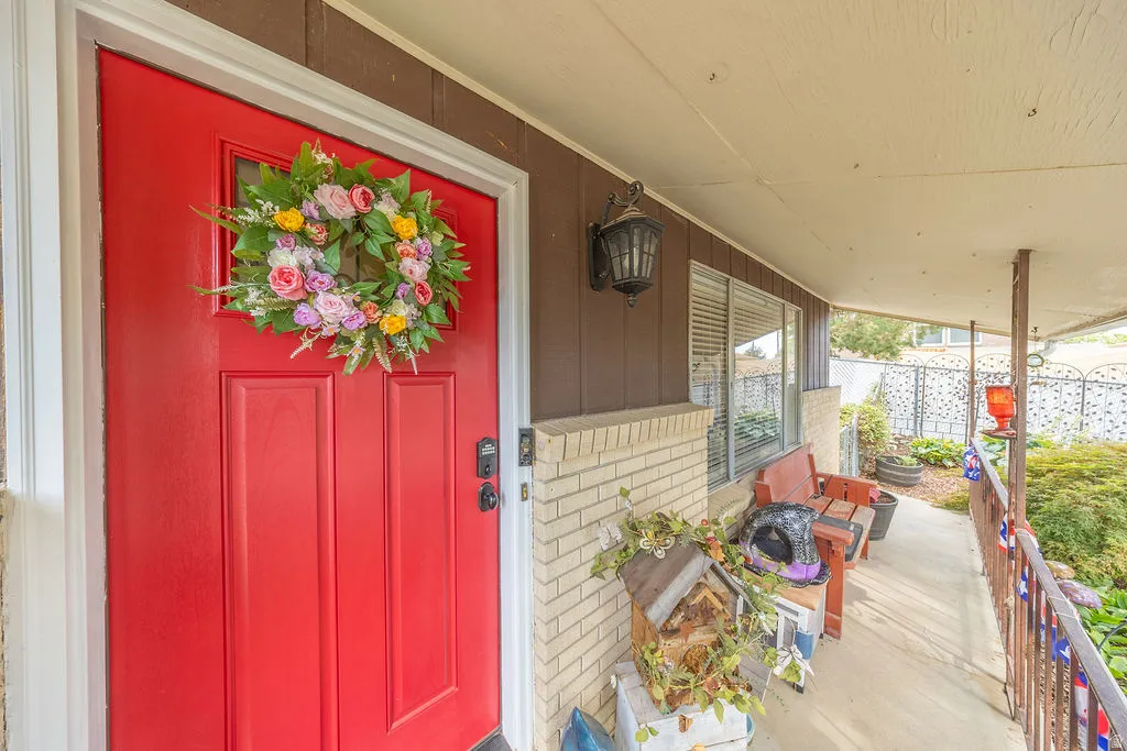 Cute covered front porch featuring a vibrant red entry door, white trim, and a decorative wall sconce