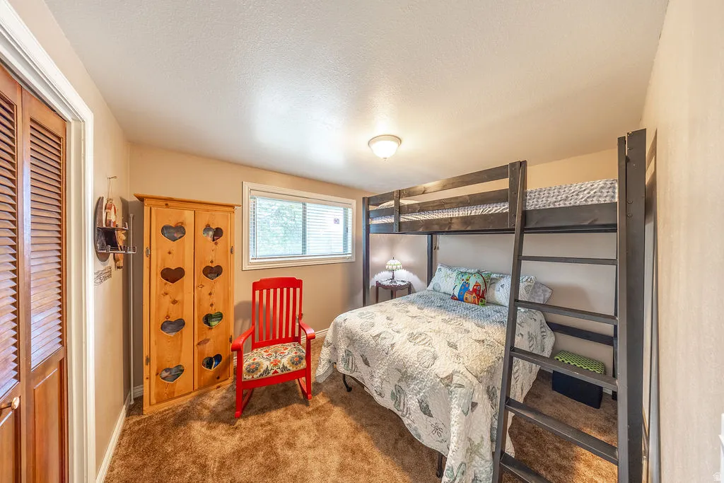 Carpeted room featuring  a window with horizontal blinds and a louvered bi-fold closet doors.