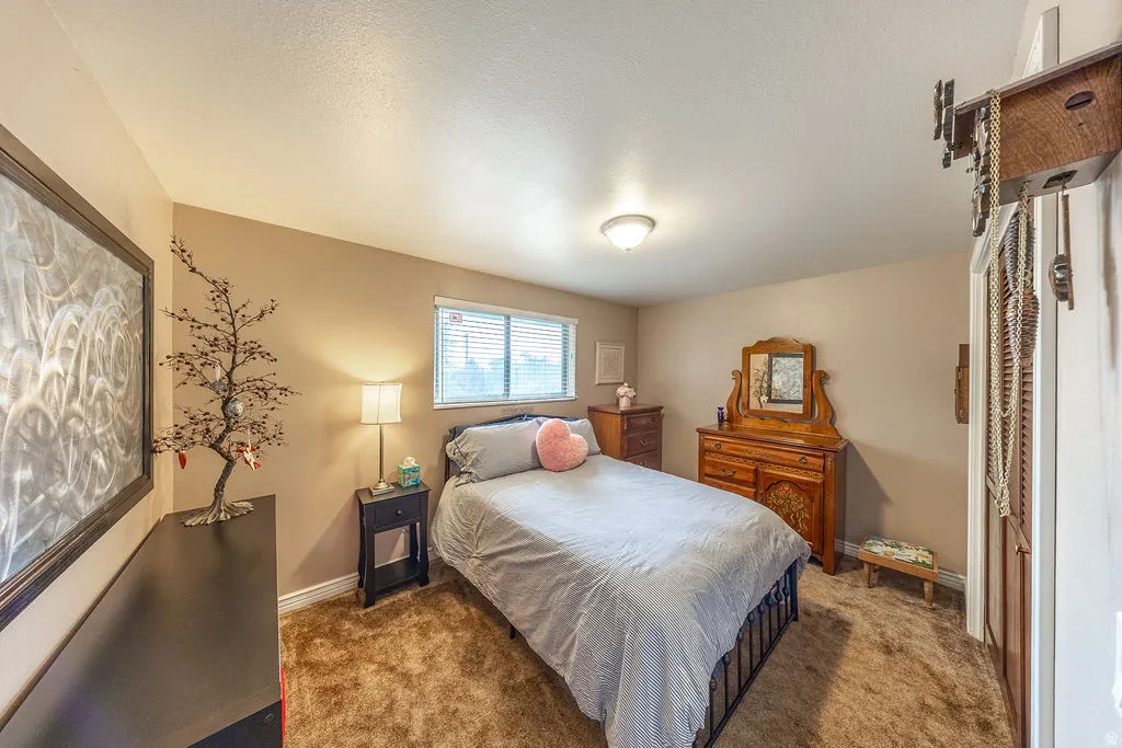 Carpeted room featuring a window with horizontal blinds, and a built-in closet with louvered bifold doors