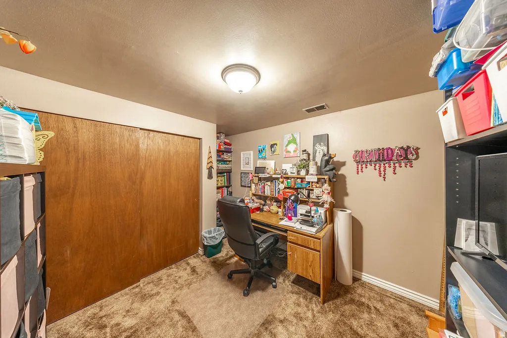 Room featuring a built-in closet with wood-finish sliding doors, carpet flooring, and another door that opens in the room to storage under the staircase.  Currently used as an office.