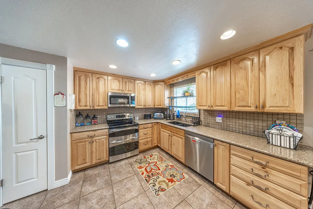 Kitchen featuring light wood cabinetry, stone-finish countertops, stainless steel appliances, and a tiled backsplash