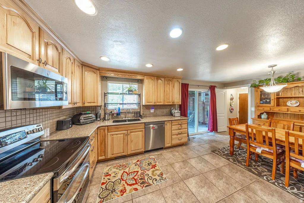 Kitchen and dining area featuring light wood cabinetry, stainless steel appliances, tile flooring, and silestone countertops