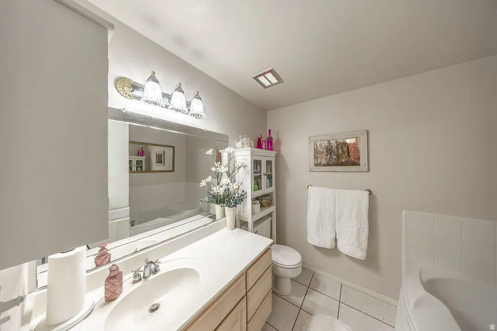 Bathroom featuring a spacious vanity with a single basin sink, an expansive wall-mounted mirror, overhead vanity lighting, a large built-in tub, and tile flooring