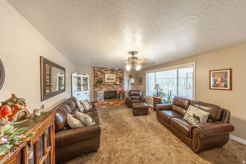 Living area featuring a brick fireplace, a large picture window, and a ceiling fan and neutral carpet.
