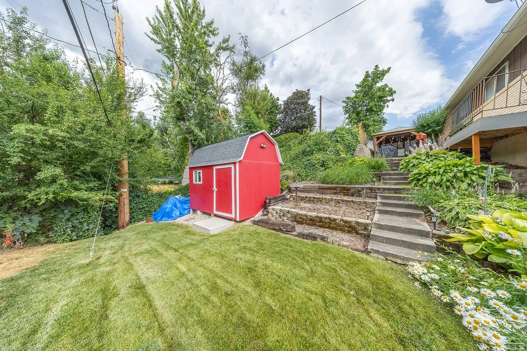 Backyard featuring a red barn-style shed on a concrete pad, tiered landscaping with concrete stairs, and mature trees