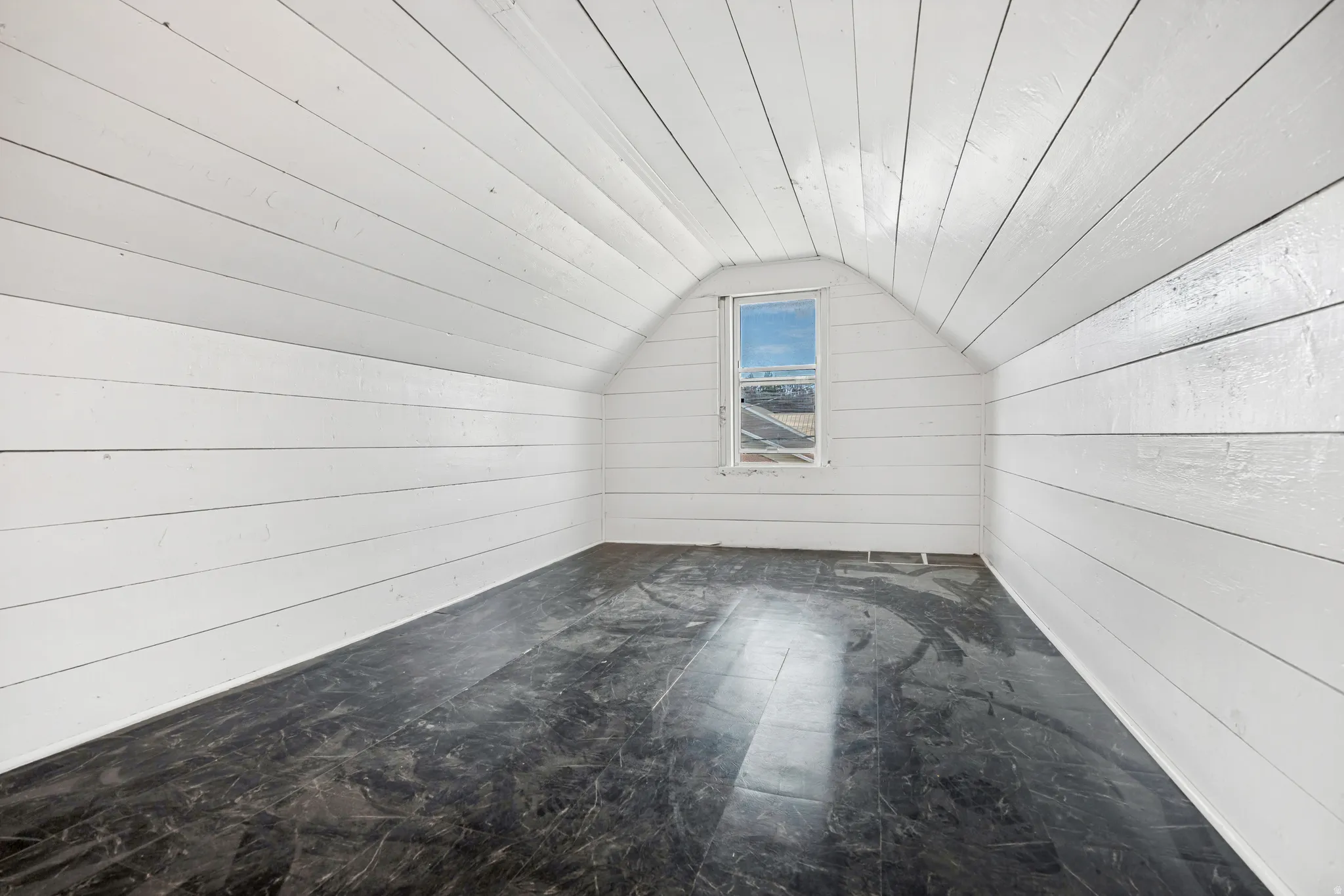 Attic space featuring white plank walls, a vaulted ceiling, and dark flooring