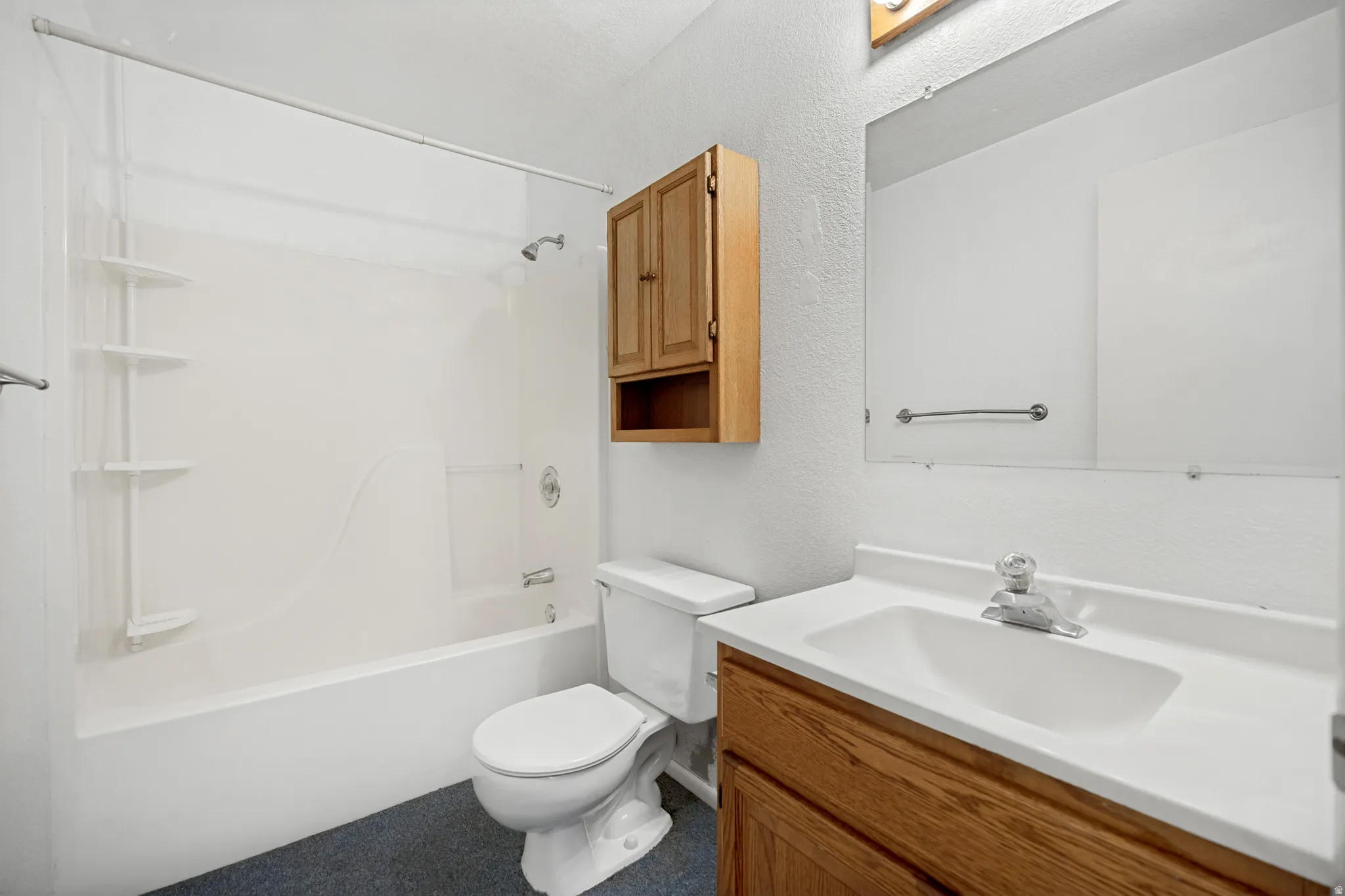 Bathroom featuring a white tub and shower combination with integrated shelving, wood-finish vanity with a white countertop and integrated sink, wall-mounted mirror, and overhead wood-finish cabinetry