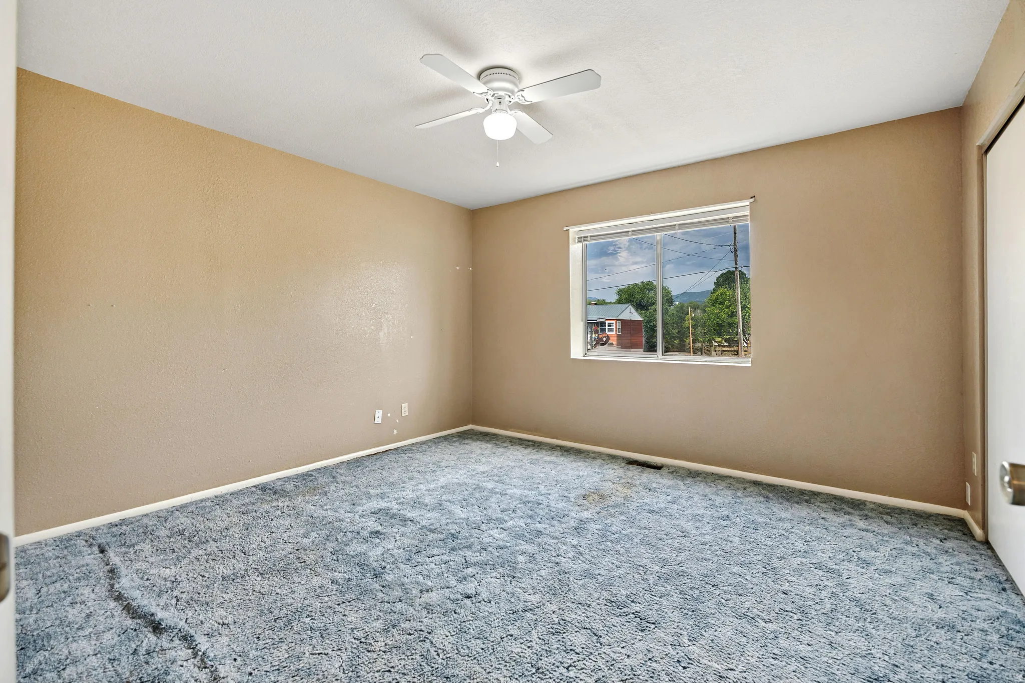 Carpeted room featuring a ceiling fan with light fixture, neutral wall tones, and a window providing exterior views
