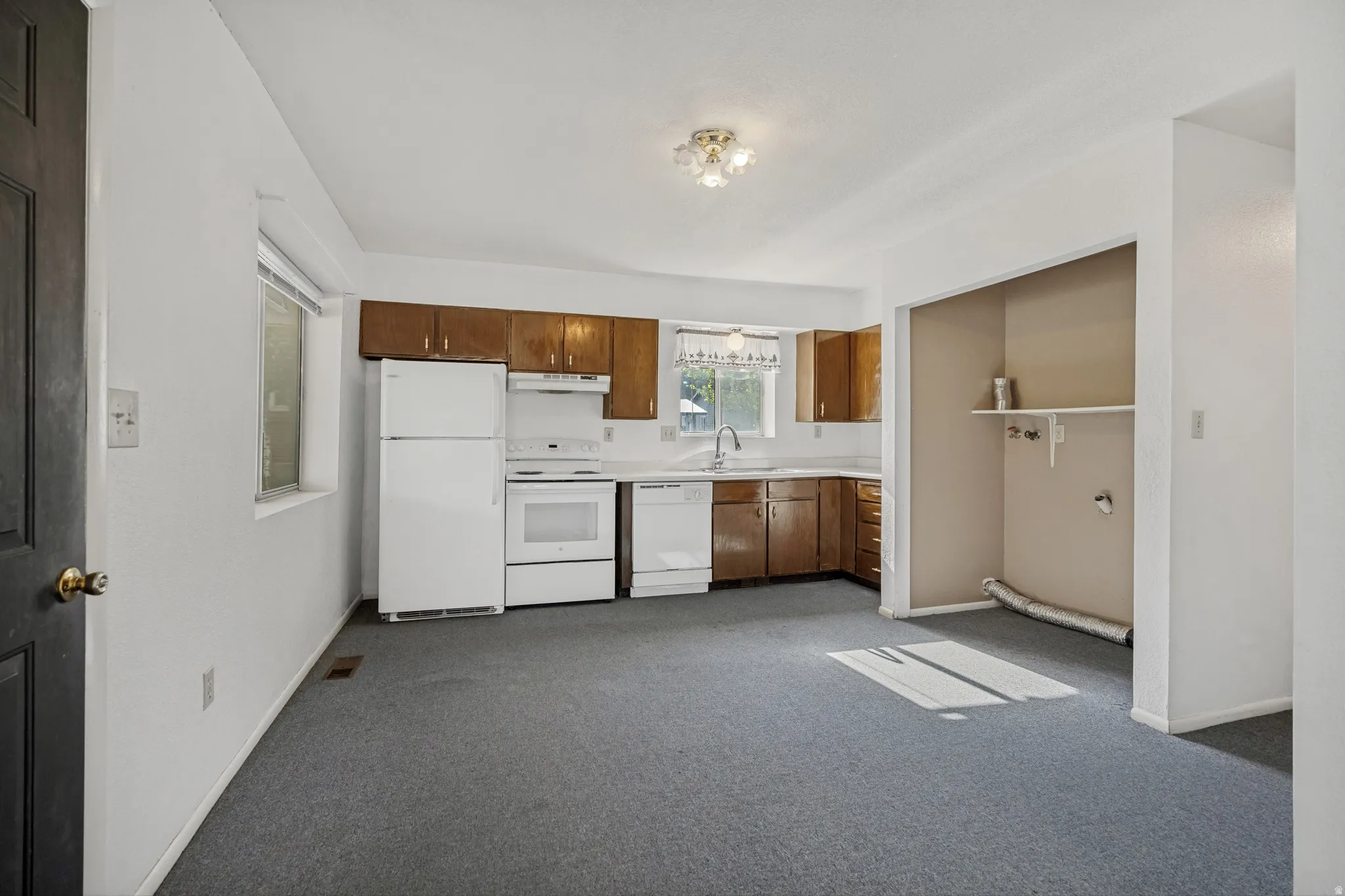 Kitchen area featuring wood cabinetry, white appliances, and a built-in laundry alcove with shelving.