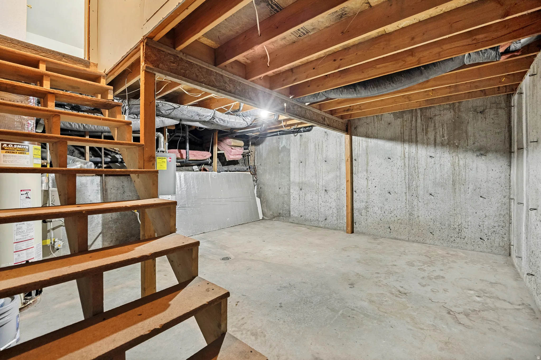 Unfinished basement space featuring exposed wood joists and concrete flooring