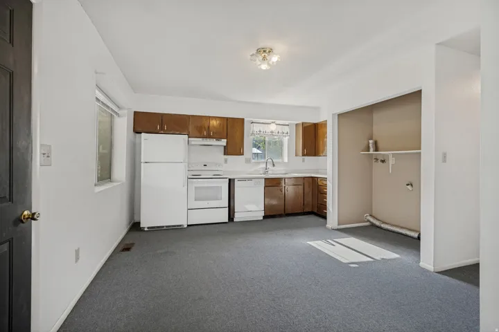 Kitchen area featuring wood cabinetry, white appliances, and a built-in laundry alcove with shelving.