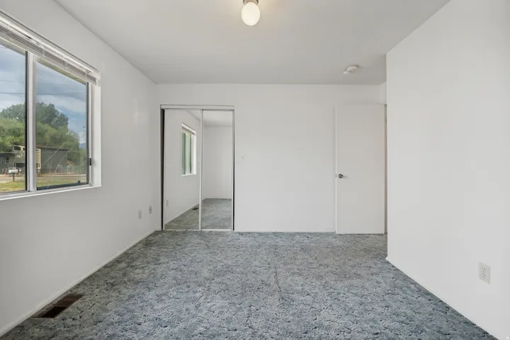Spacious room featuring a large window, light blue carpet, white walls, and a mirrored closet door