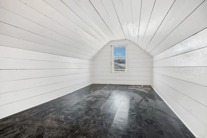 Attic space featuring white plank walls, a vaulted ceiling, and dark flooring