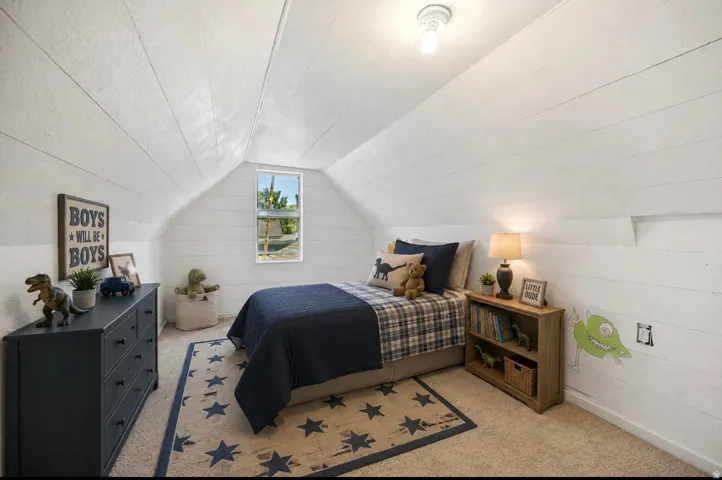 Vaulted ceiling with horizontal paneling, wall-mounted light fixture, carpeted flooring, and a single window